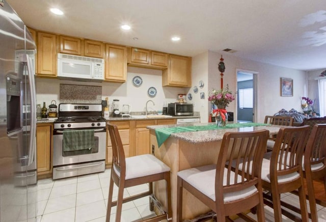 kitchen with sink, appliances with stainless steel finishes, a center island, light stone counters, and light tile patterned flooring