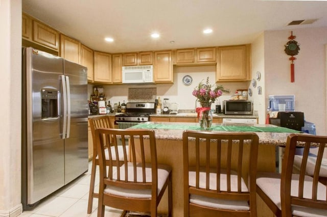 kitchen with light brown cabinetry, light tile patterned floors, stainless steel appliances, and a kitchen breakfast bar