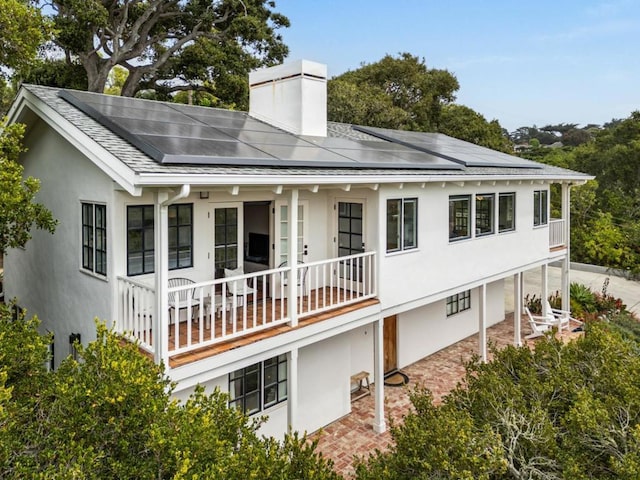 rear view of property featuring covered porch and solar panels