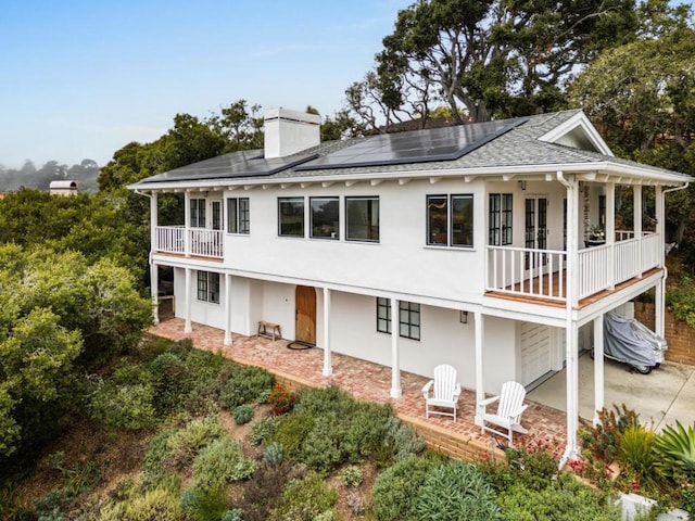 rear view of property with a balcony, solar panels, and a garage