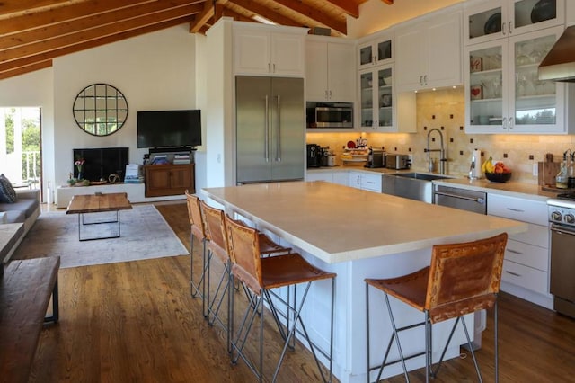 kitchen featuring tasteful backsplash, vaulted ceiling with beams, appliances with stainless steel finishes, a kitchen breakfast bar, and white cabinets