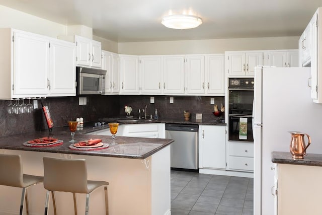 kitchen featuring tile patterned flooring, a breakfast bar, kitchen peninsula, appliances with stainless steel finishes, and white cabinets