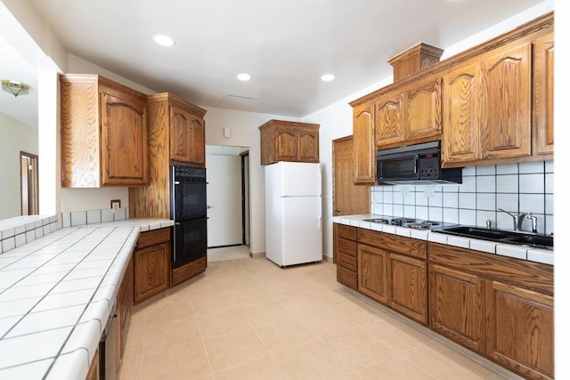 kitchen featuring tile counters, sink, decorative backsplash, and black appliances