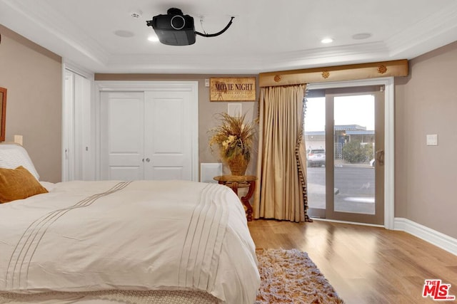 bedroom featuring a tray ceiling, a closet, access to exterior, ornamental molding, and light hardwood / wood-style flooring