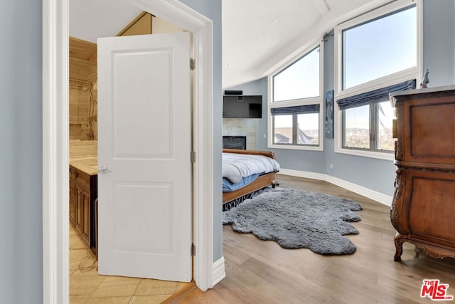 bedroom featuring light wood-type flooring, vaulted ceiling, a tile fireplace, and connected bathroom