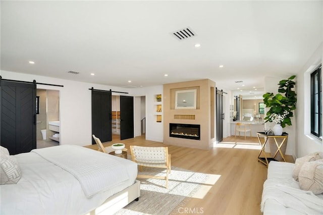 bedroom featuring a fireplace, ensuite bathroom, a barn door, and light wood-type flooring