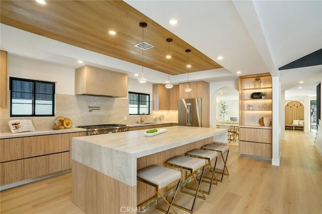 kitchen with a kitchen bar, a large island, high end fridge, hanging light fixtures, and wall chimney exhaust hood