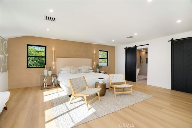 bedroom featuring a barn door, light wood-type flooring, and multiple windows