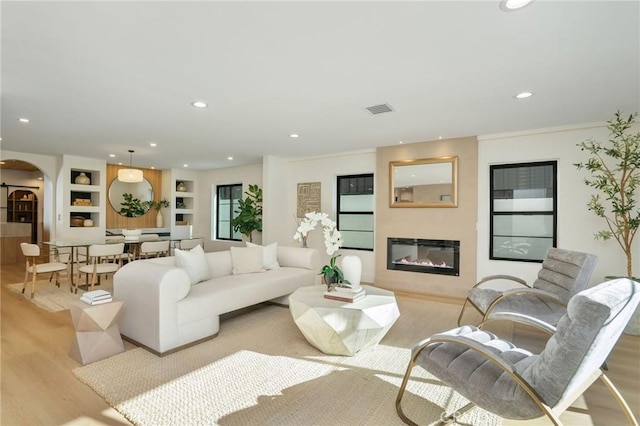 living room with ornamental molding, built in features, and light hardwood / wood-style flooring