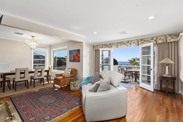 living room featuring plenty of natural light, wood-type flooring, ornamental molding, and an inviting chandelier