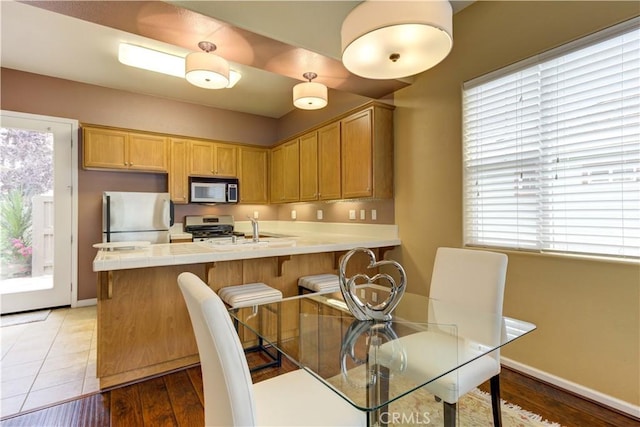 kitchen with light brown cabinetry, dark hardwood / wood-style floors, a kitchen breakfast bar, and stainless steel appliances