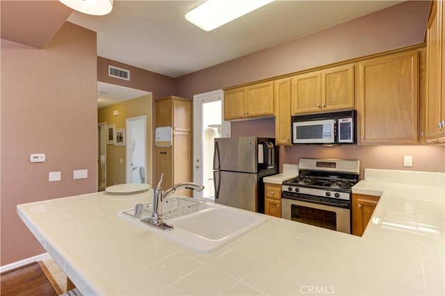 kitchen with tile counters, kitchen peninsula, appliances with stainless steel finishes, and sink