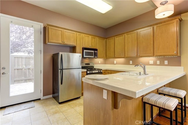 kitchen featuring a kitchen bar, kitchen peninsula, appliances with stainless steel finishes, tile counters, and sink