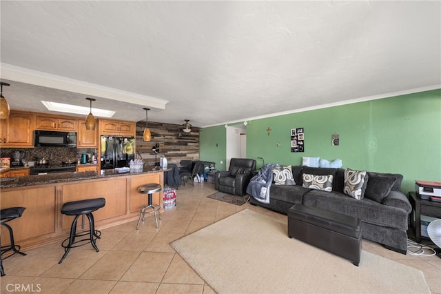 living room featuring ceiling fan, light tile patterned flooring, wooden walls, and ornamental molding