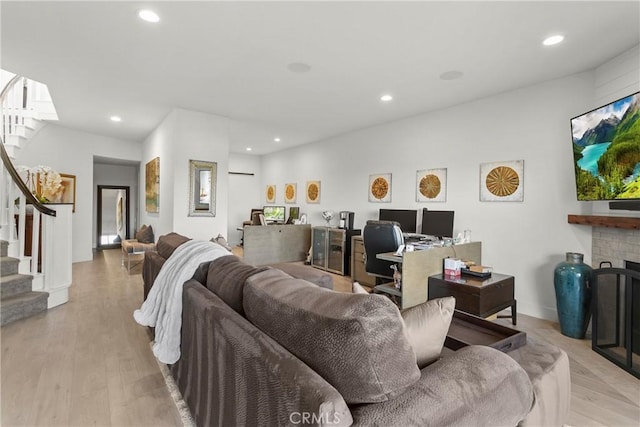 living room featuring a brick fireplace, light wood-style flooring, stairs, and recessed lighting