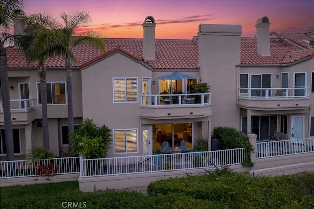 back of property at dusk featuring fence, a tiled roof, and stucco siding