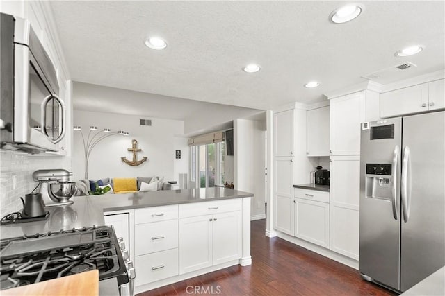 kitchen featuring visible vents, a peninsula, white cabinets, appliances with stainless steel finishes, and dark wood-style floors