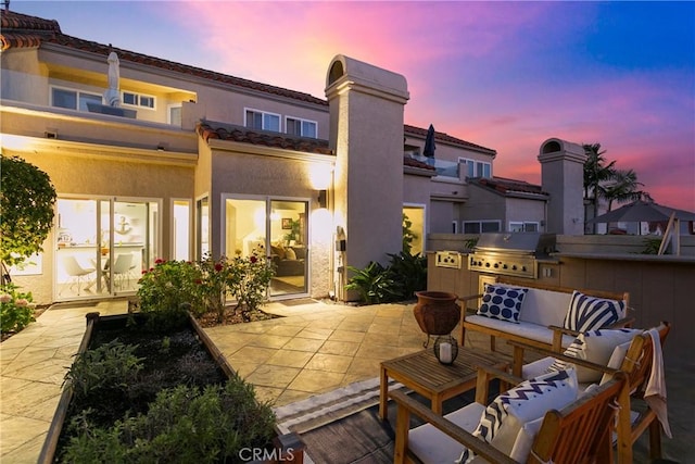 patio terrace at dusk with a grill, an outdoor kitchen, and an outdoor living space