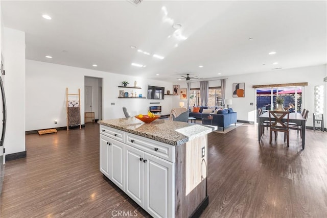 kitchen with light stone counters, white cabinetry, dark hardwood / wood-style floors, and a kitchen island