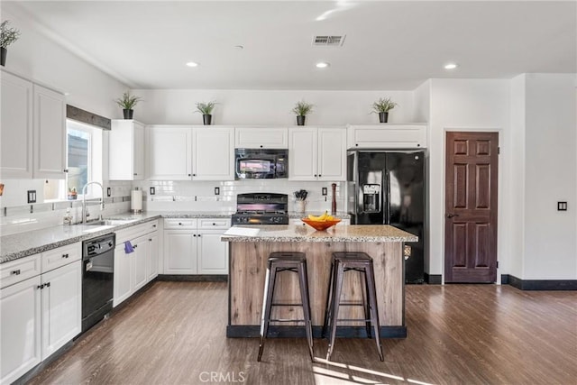 kitchen featuring a kitchen island, black appliances, sink, white cabinetry, and light stone countertops