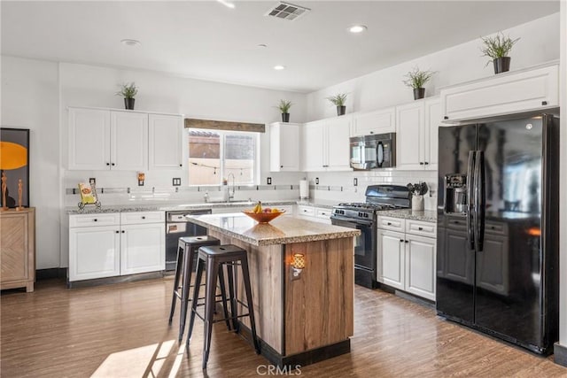 kitchen featuring dark hardwood / wood-style floors, a center island, black appliances, white cabinetry, and a breakfast bar area