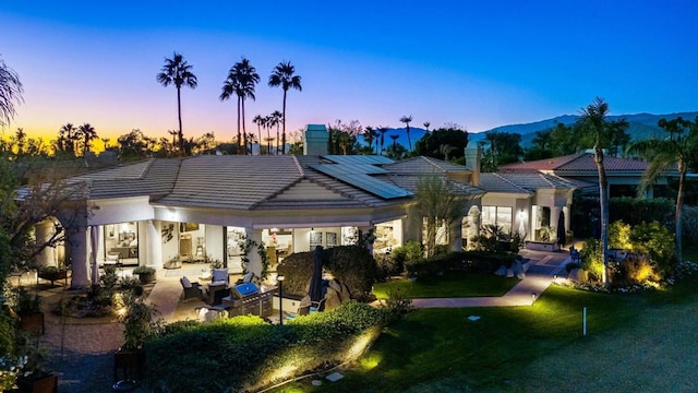 back house at dusk featuring a lawn, solar panels, a mountain view, and a patio