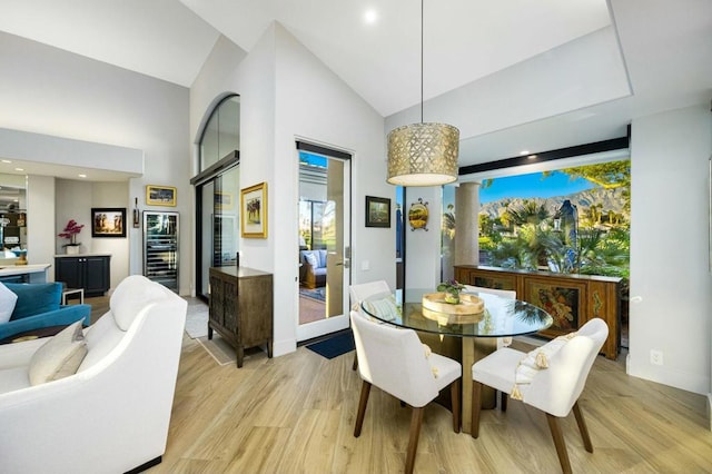 dining space featuring wine cooler, light hardwood / wood-style flooring, and high vaulted ceiling