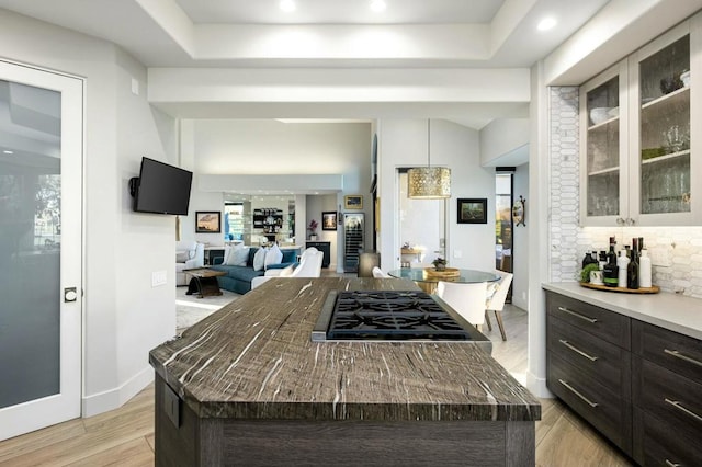 kitchen with a center island, decorative backsplash, light hardwood / wood-style floors, stainless steel gas cooktop, and dark brown cabinets