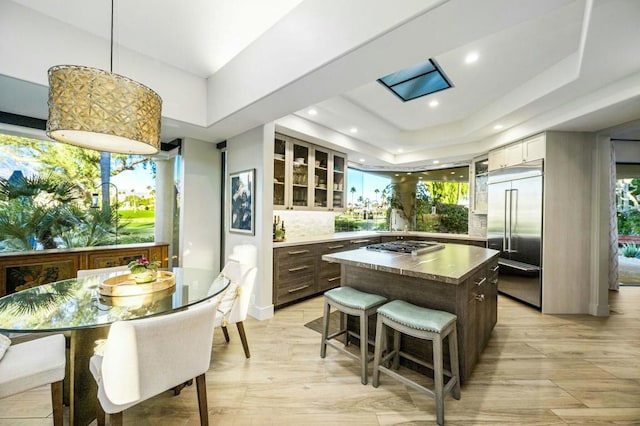 kitchen with dark brown cabinetry, appliances with stainless steel finishes, a center island, decorative backsplash, and a tray ceiling