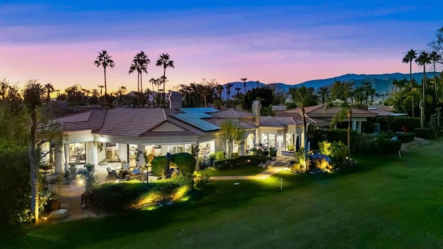 back house at dusk with a lawn and a mountain view