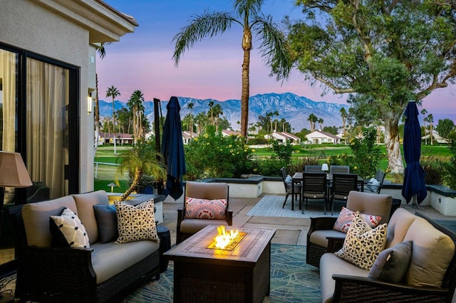 patio terrace at dusk featuring a mountain view and an outdoor living space with a fire pit