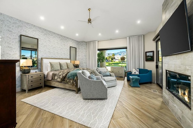 bedroom with ceiling fan, a tile fireplace, and light hardwood / wood-style flooring