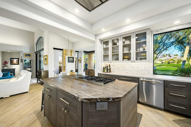 kitchen with appliances with stainless steel finishes, a kitchen island, decorative backsplash, light hardwood / wood-style floors, and dark brown cabinets