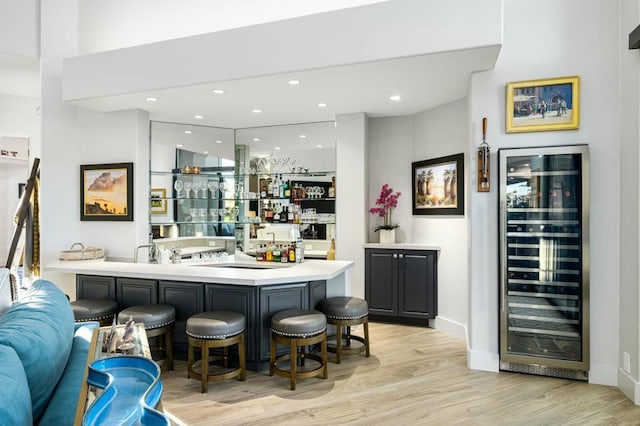 bar with beverage cooler, white cabinetry, and light hardwood / wood-style flooring