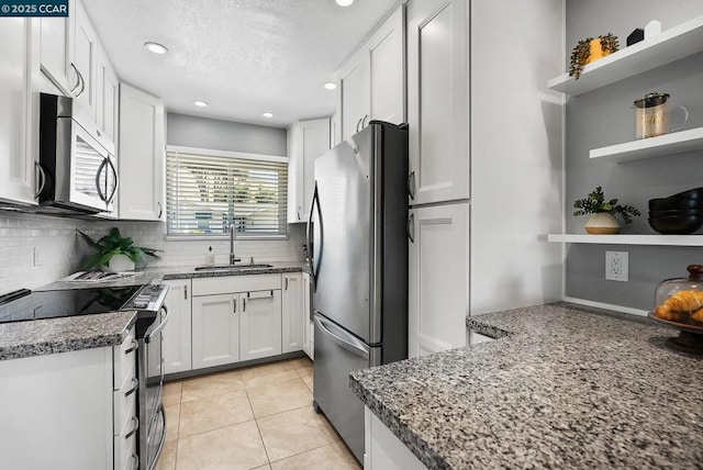 kitchen with stainless steel appliances, light tile patterned flooring, dark stone counters, white cabinets, and sink