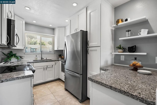 kitchen with light tile patterned floors, appliances with stainless steel finishes, dark stone countertops, white cabinets, and sink