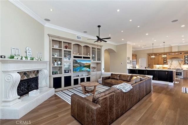 living room with ceiling fan, crown molding, hardwood / wood-style floors, and a tile fireplace