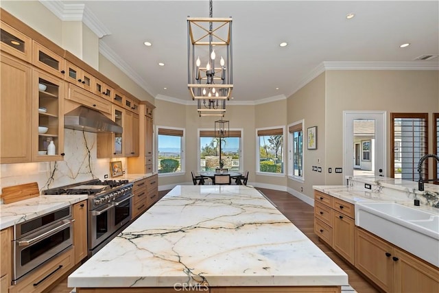 kitchen with a center island, wall chimney exhaust hood, stainless steel appliances, hanging light fixtures, and ornamental molding