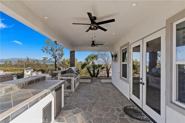 view of patio / terrace featuring a mountain view, ceiling fan, an outdoor kitchen, french doors, and area for grilling