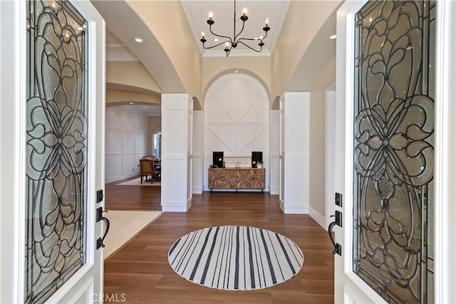 entryway with dark hardwood / wood-style flooring, an inviting chandelier, ornamental molding, and ornate columns