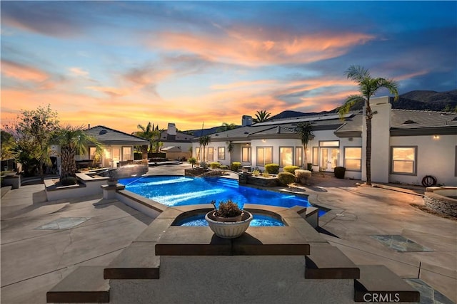 pool at dusk with an in ground hot tub, a patio area, and pool water feature