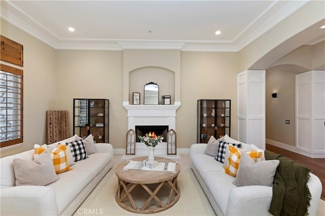 living room with wood-type flooring, a large fireplace, and ornamental molding