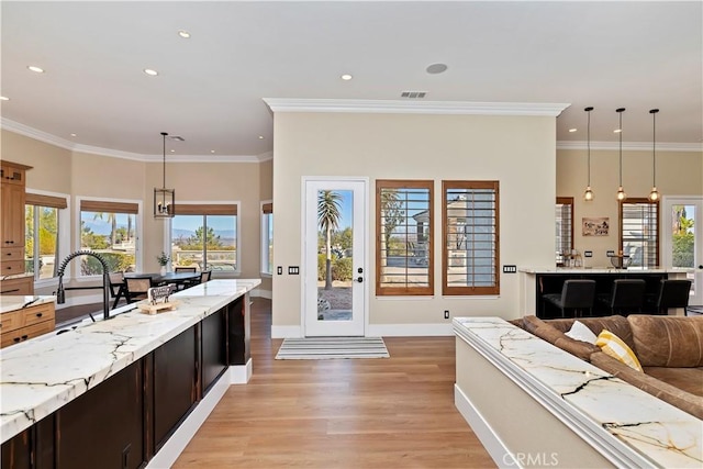 kitchen with pendant lighting, light stone countertops, crown molding, light hardwood / wood-style flooring, and sink