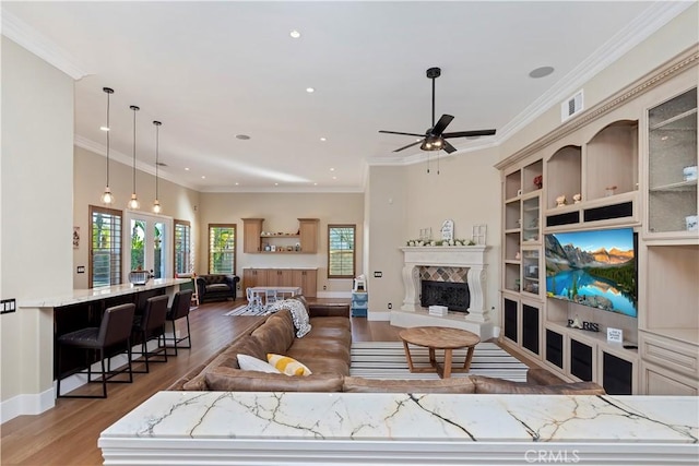 living room with a high end fireplace, ceiling fan, built in features, hardwood / wood-style flooring, and crown molding