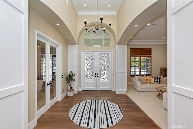 foyer entrance featuring hardwood / wood-style flooring, crown molding, french doors, and an inviting chandelier