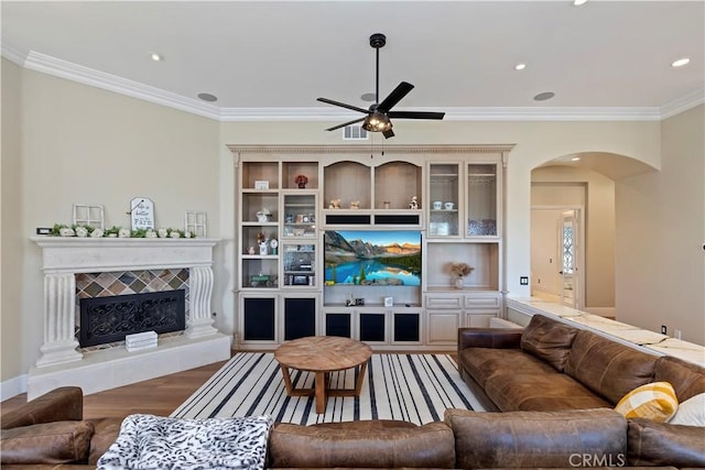 living room featuring ceiling fan, hardwood / wood-style floors, a tile fireplace, and ornamental molding