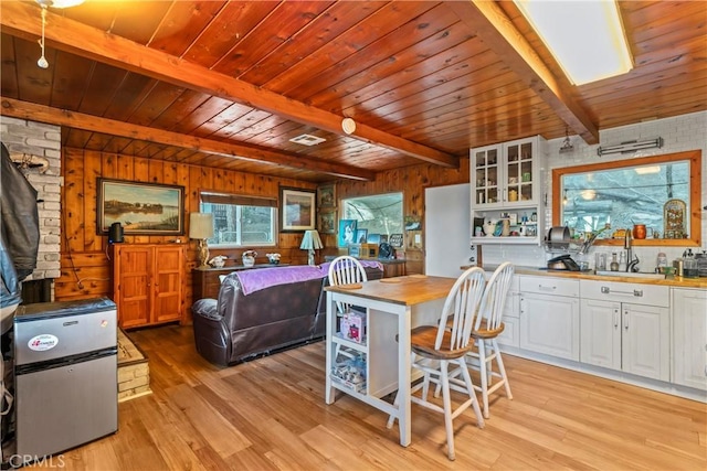 kitchen with white cabinetry, sink, wood walls, a breakfast bar, and beam ceiling