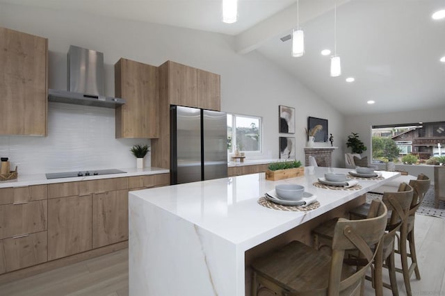 kitchen with tasteful backsplash, wall chimney range hood, vaulted ceiling with beams, hanging light fixtures, and stainless steel fridge