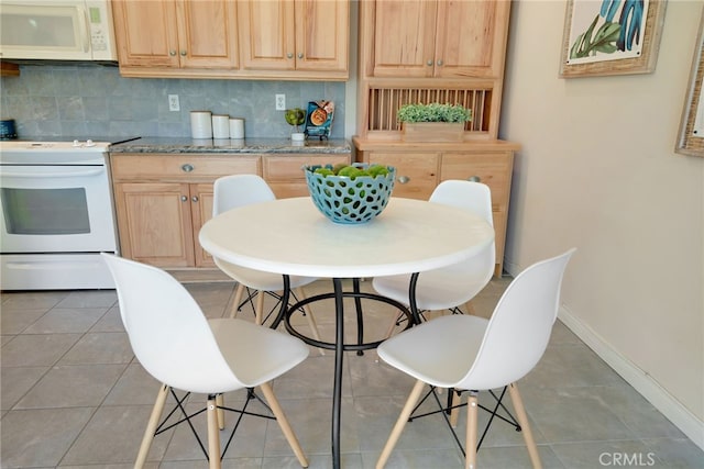 kitchen featuring dark tile patterned floors, light brown cabinetry, white appliances, and tasteful backsplash