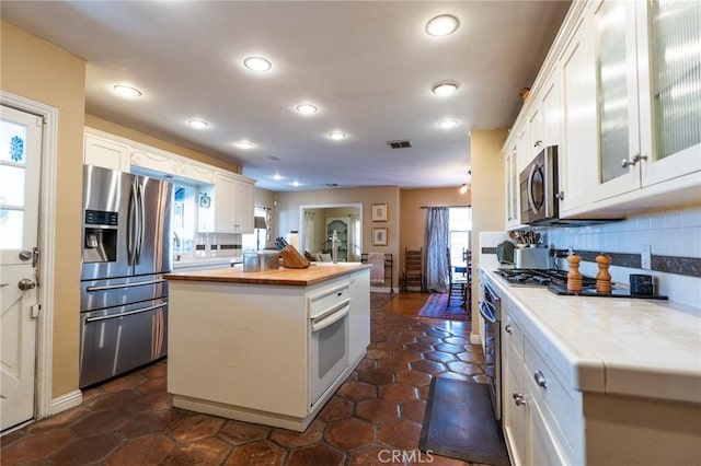 kitchen featuring wooden counters, a kitchen island, decorative backsplash, white cabinetry, and appliances with stainless steel finishes